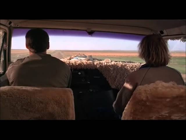 The backs of Jeff Daniels and Jim Carrey inside the front seats of their car with the Rocky Mountains on the horizon