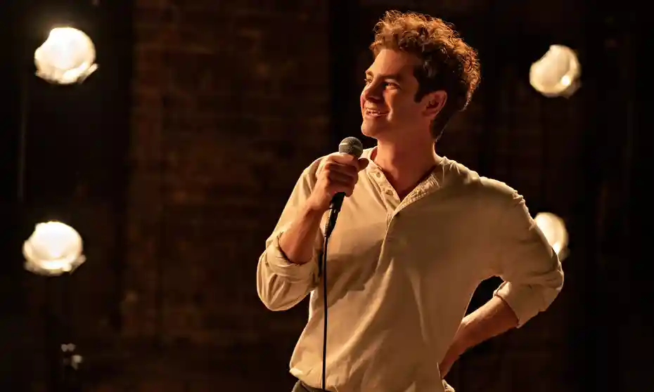 Andrew Garfield as Jonathan Larson holding a microphone