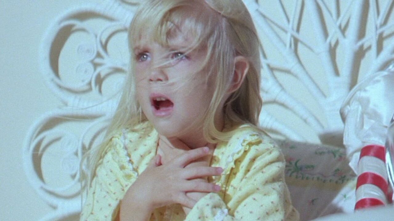 The frightened Carol Anne clasps her hands in bed in Poltergeist