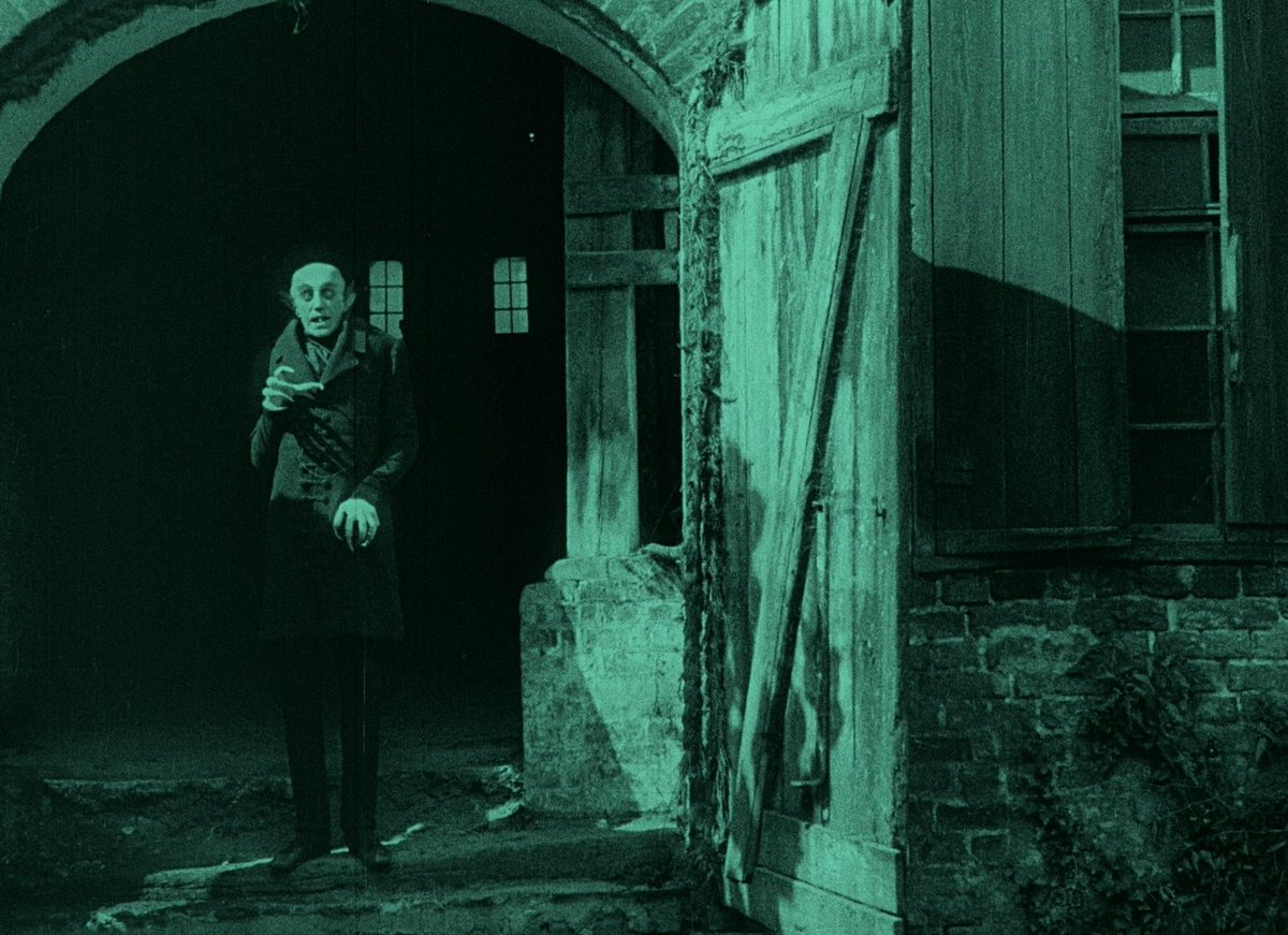 Count Orlok stands outside his open front door.