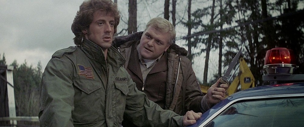 Stallone and Dennehy next to a patrol car in First Blood