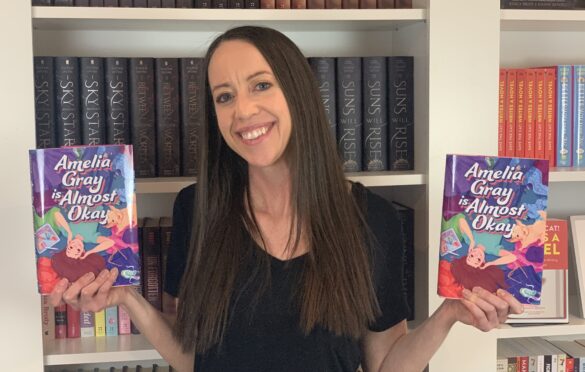 Author Jessica Brody hold her latest book, Amelia Gray is Almost Okay -- one book inn each hand