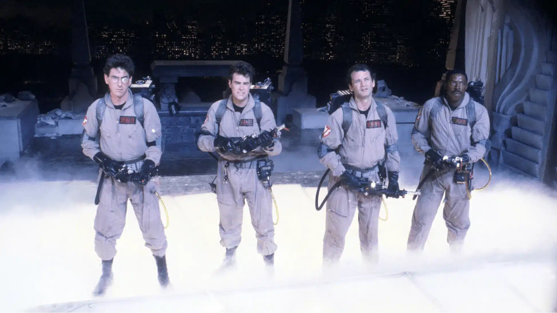 The 4 original ghostbusters in uniform with smoke surrounding their feet