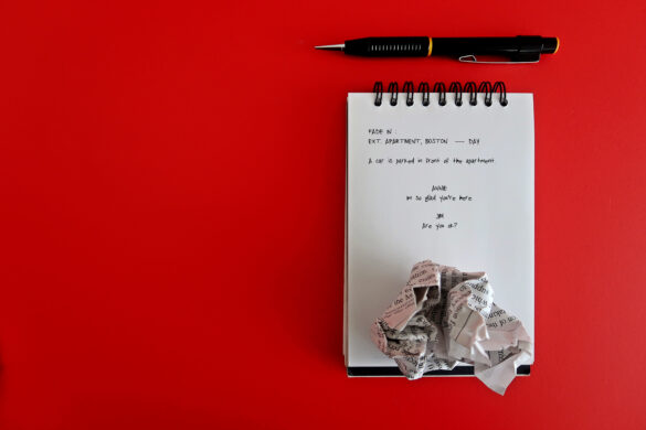 pen, notebook with the start of a screenplay, and a crumpled piece of paper