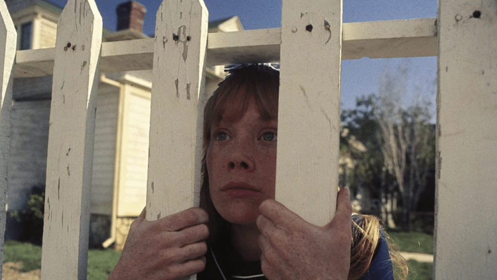 Carrie looks through a picket fence