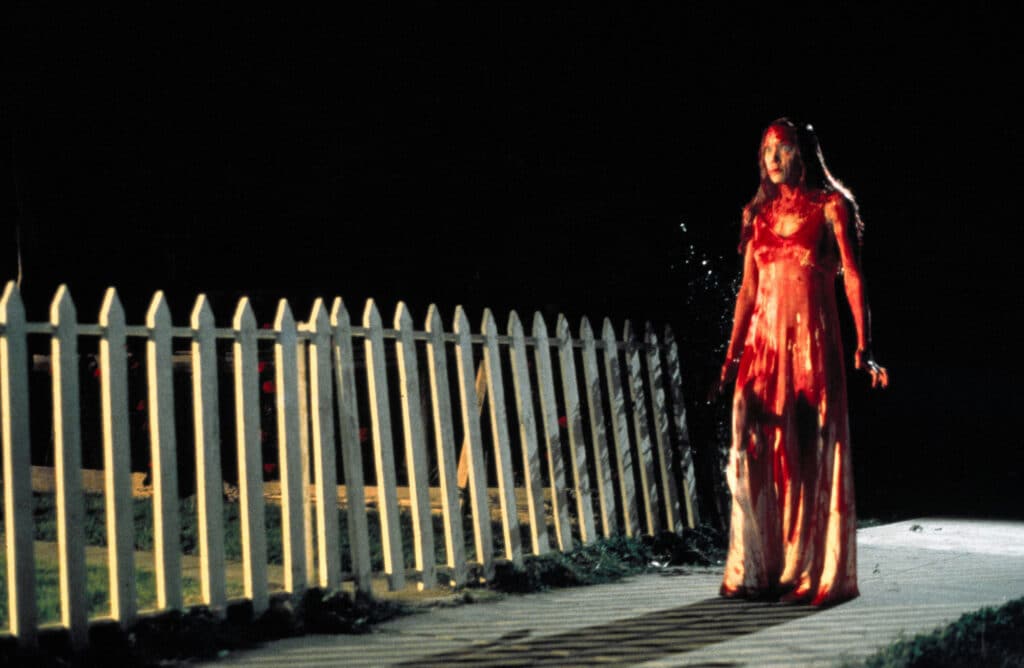 bloody Carrie walks by her home's picket fence
