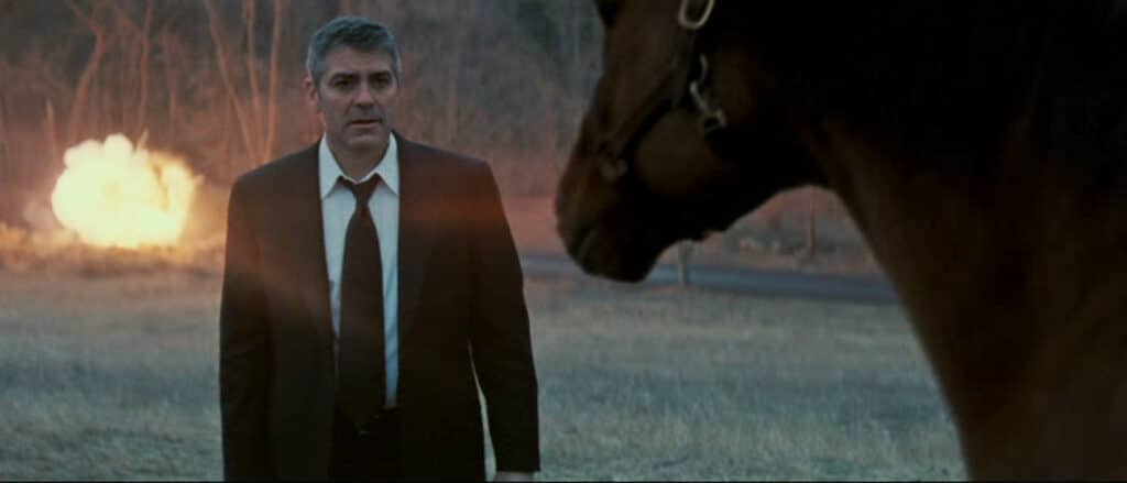 George Clooney in a field with a horse as his car burns nearby