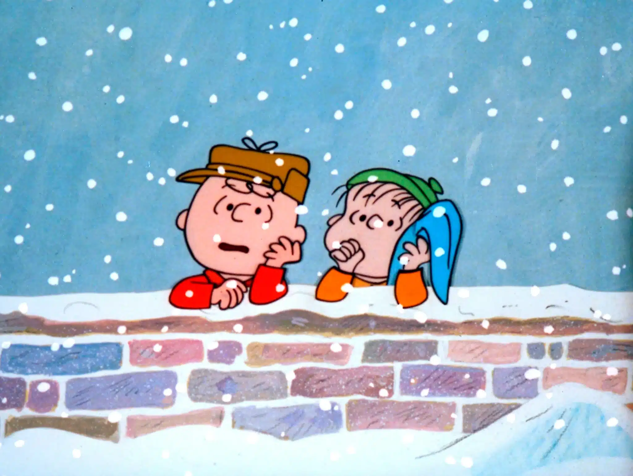 Charlie Brown and Linus talk as they lean against the snowy brick wall