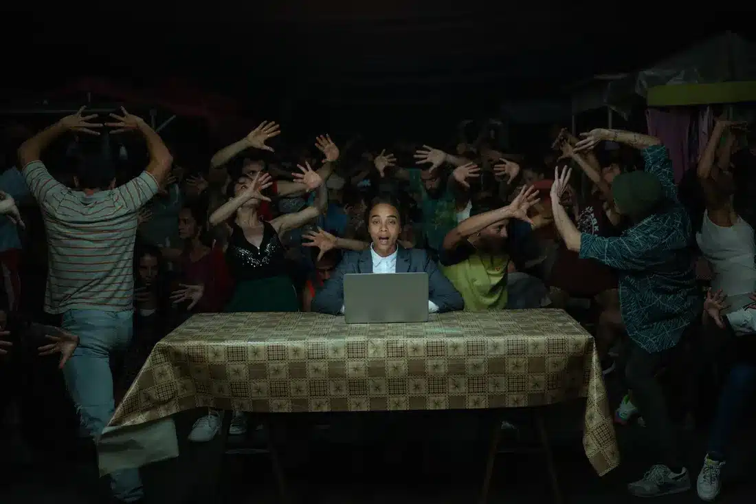 Zoe Saldana at her laptop on a table with a dozen hands surrounding her.