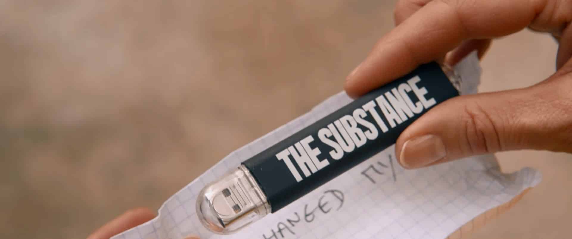 a flash drive with the words THE SUBSTANCE, held by a woman's hands