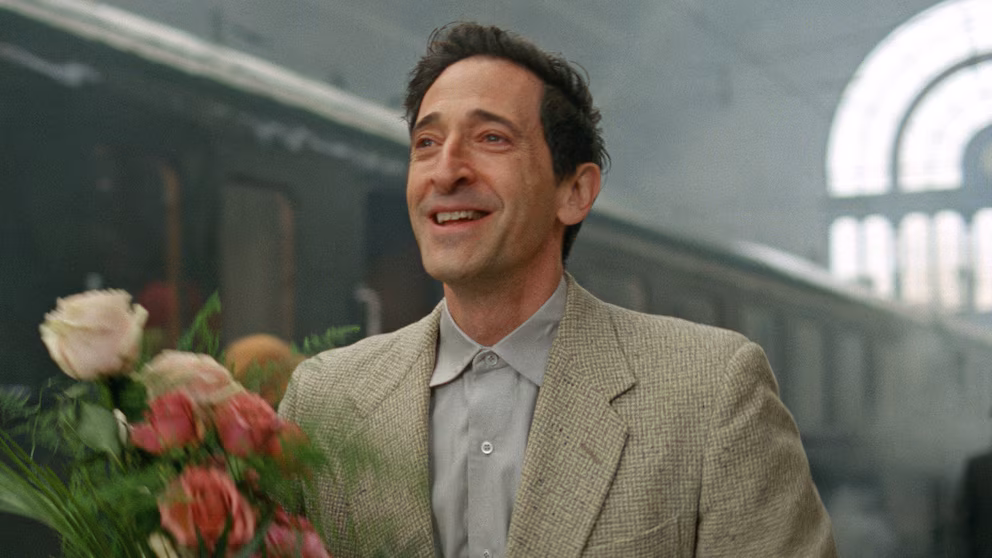 Lazlo holds a bouquet of flowers at the train station