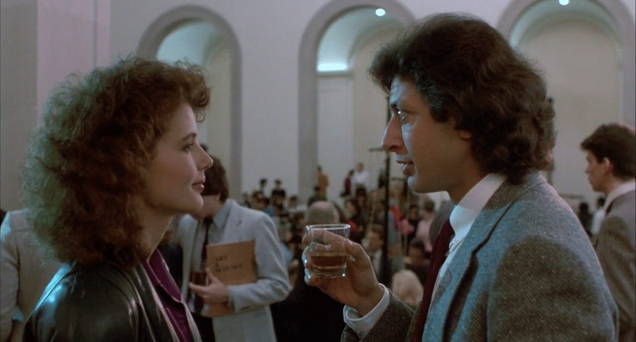 Geena Davis talking to Jeff Goldblum at a party, Goldblum holding a drink