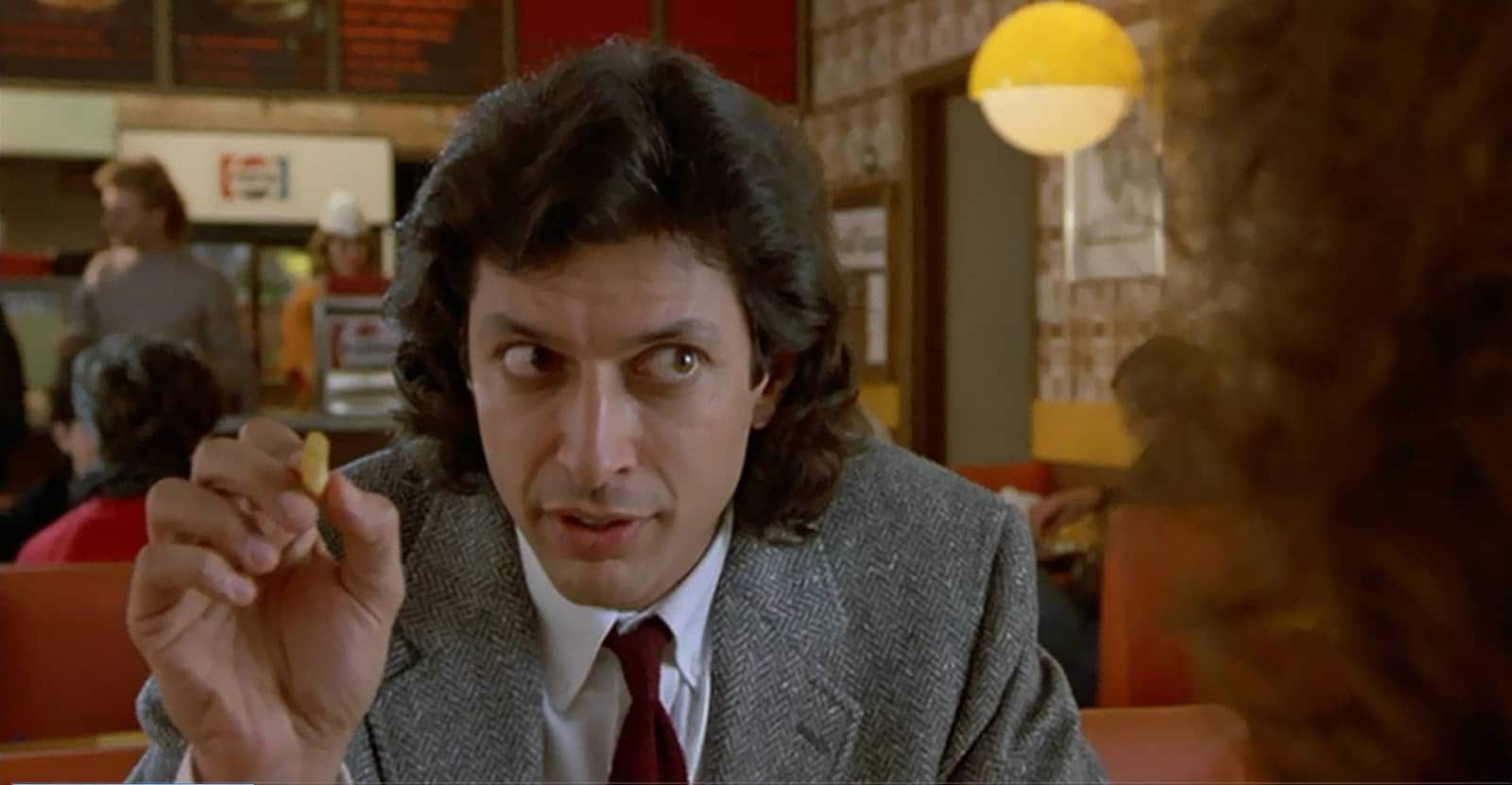 Jeff Goldblum holds a french fry while sitting in a booth at a diner