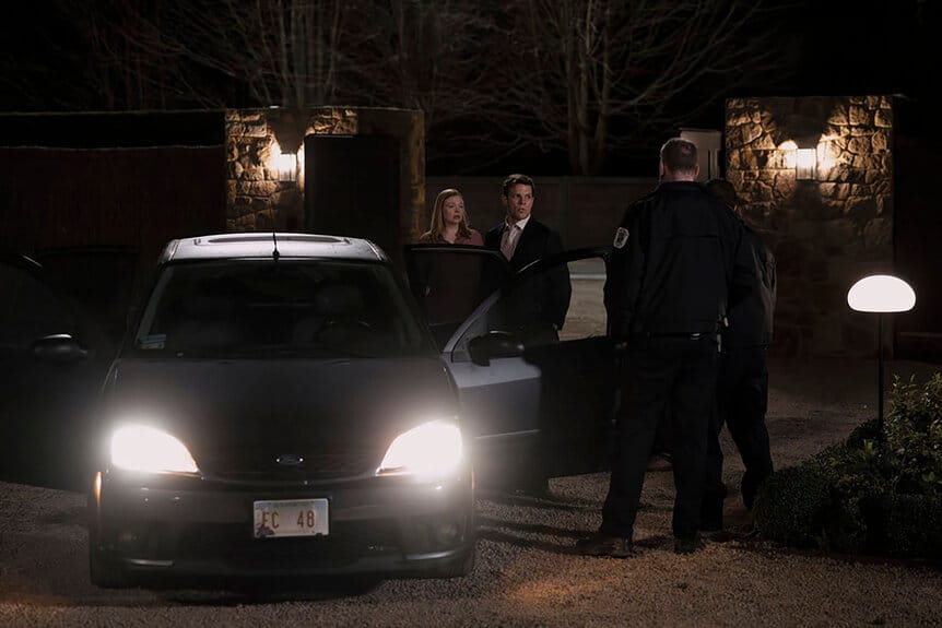 2 policeman talk to Peter and Marissa next to the police vehicle in their driveway
