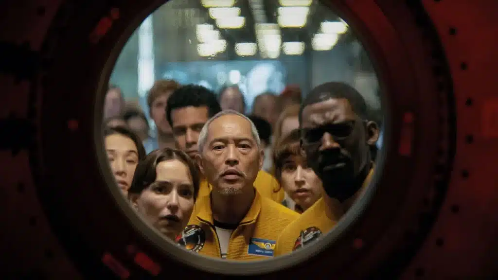 The astronauts and scientists of Project Hail Mary, seen through a glass porthole of the spaceship