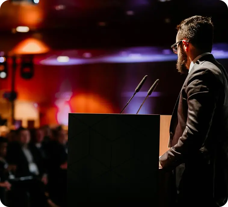 A man with glasses and a beard speaks to an audience