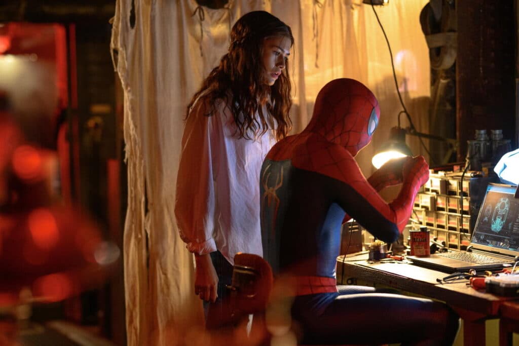 MJ stands next to the sitting Spider-Man at a desk