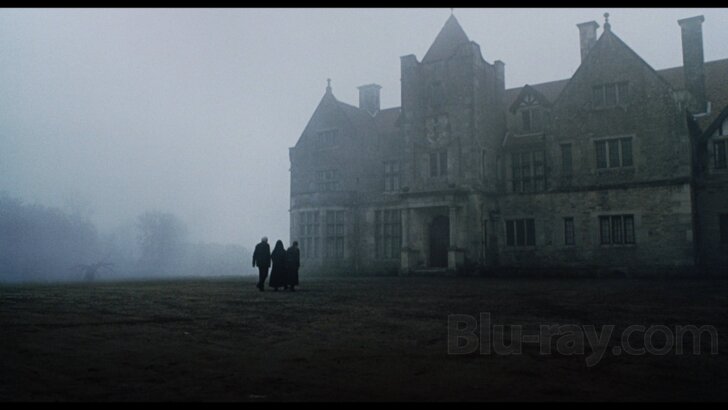 the mansion in the fog with 3 people on the front lawn